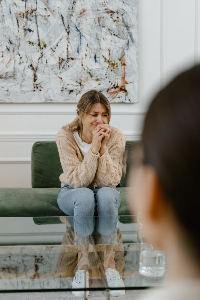 services-05 A woman sits on a sofa visibly distressed during a therapy session, hands clasped.
